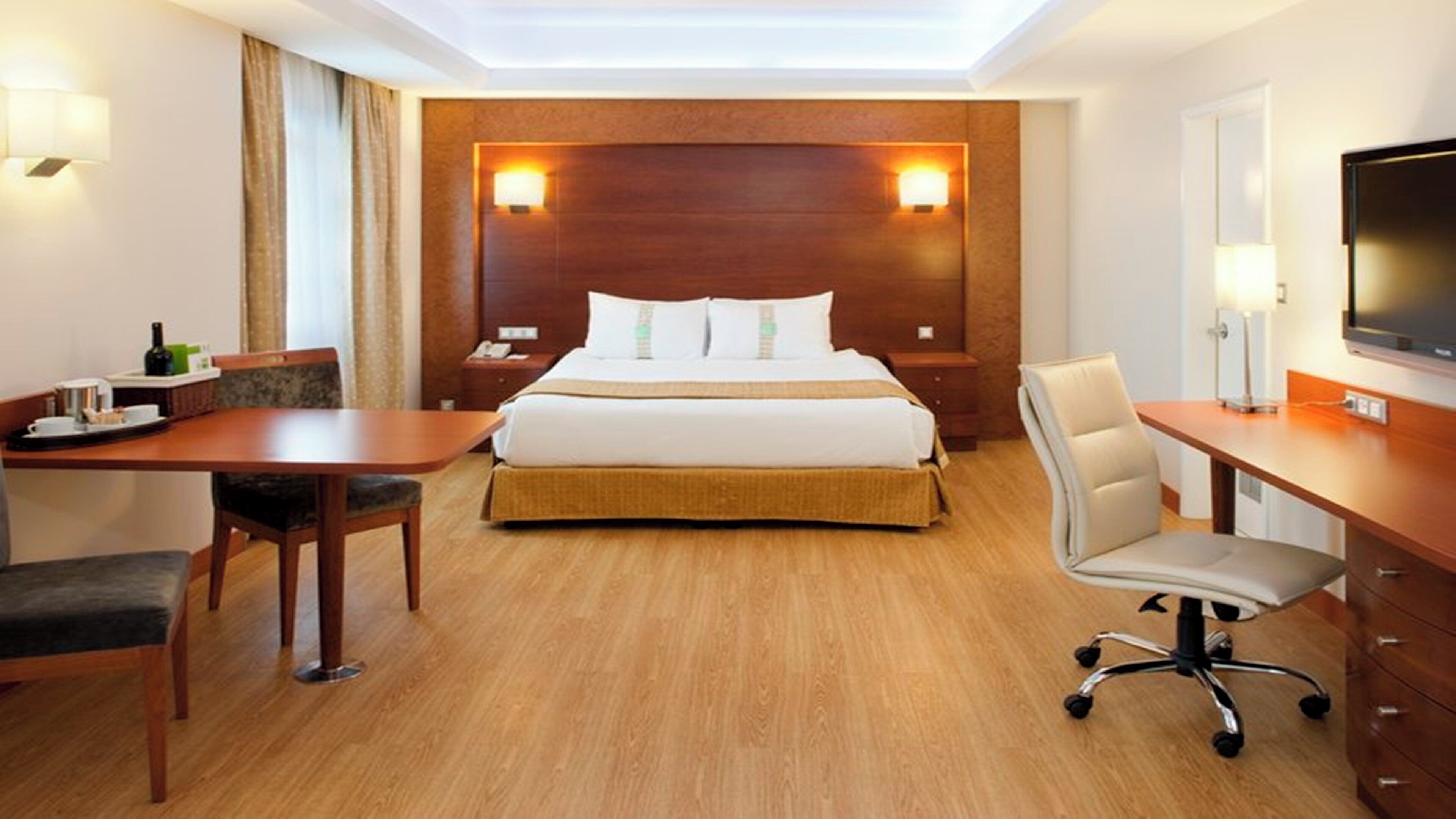 A hotel room with a bed, desk, chair, TV, and bedside lamps.