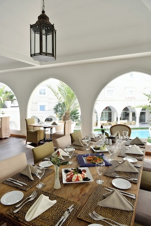 An indoor dining area with a long table set for a meal, large windows, and a view of the pool and building outside. - Holiday Inn Istanbul City by IHG (Istanbul)