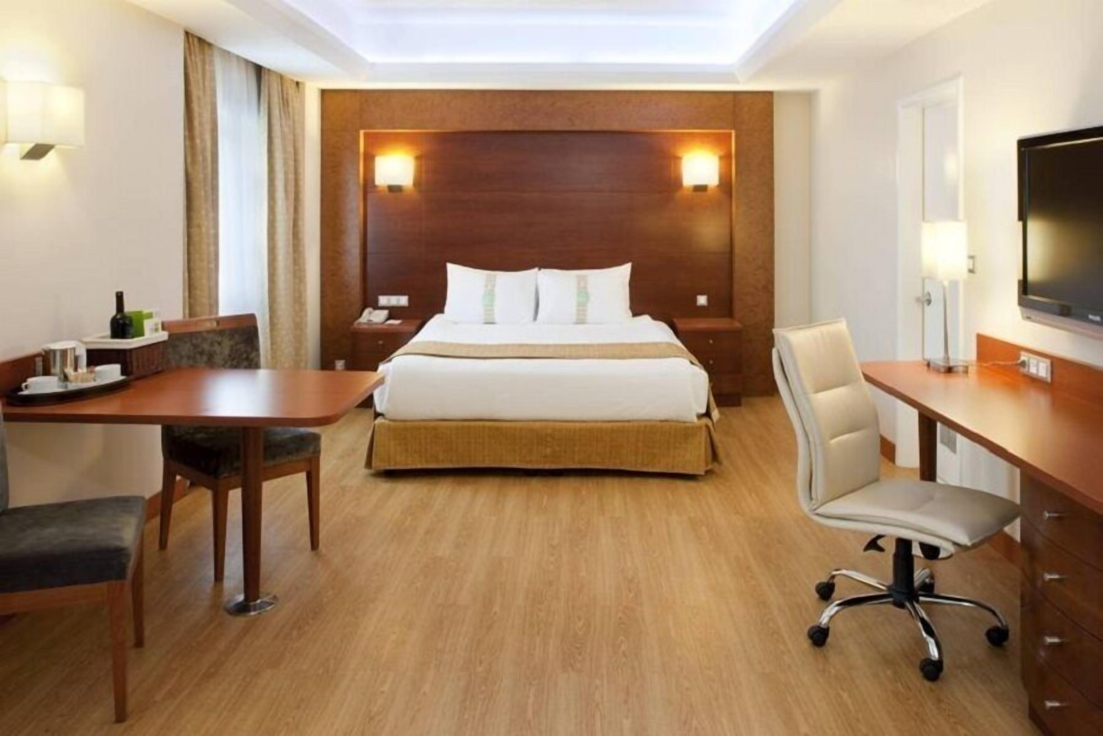 A hotel room with a large bed, a desk with a chair, a television, and a lamp.