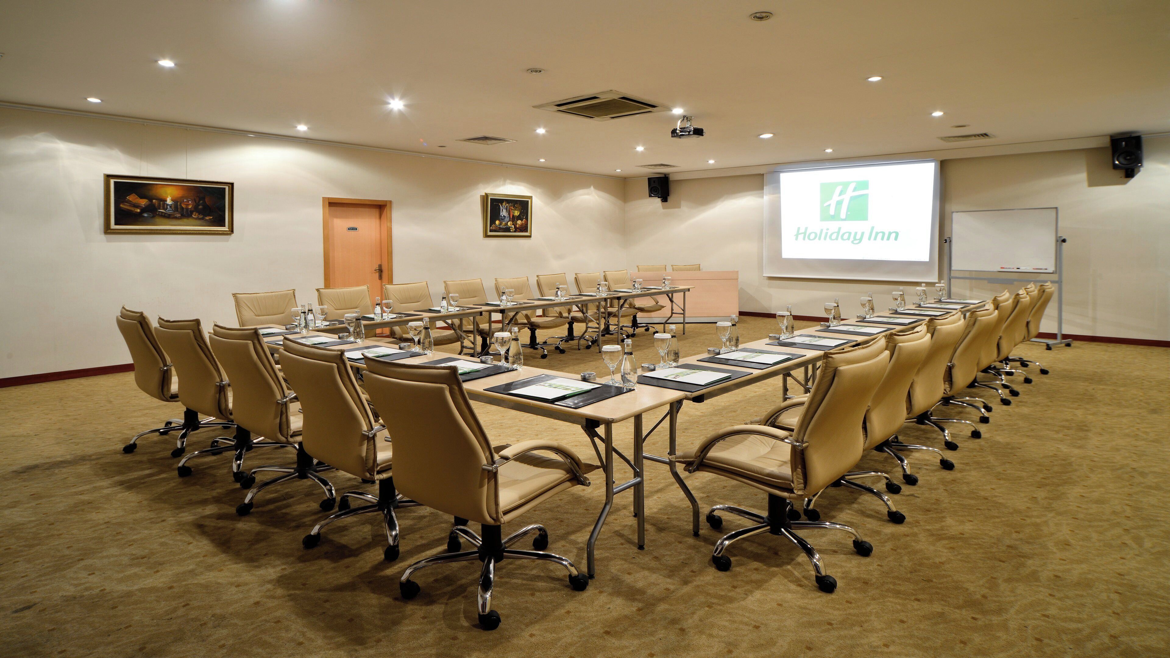 A conference room with a long table, chairs, a projector screen, and a whiteboard.