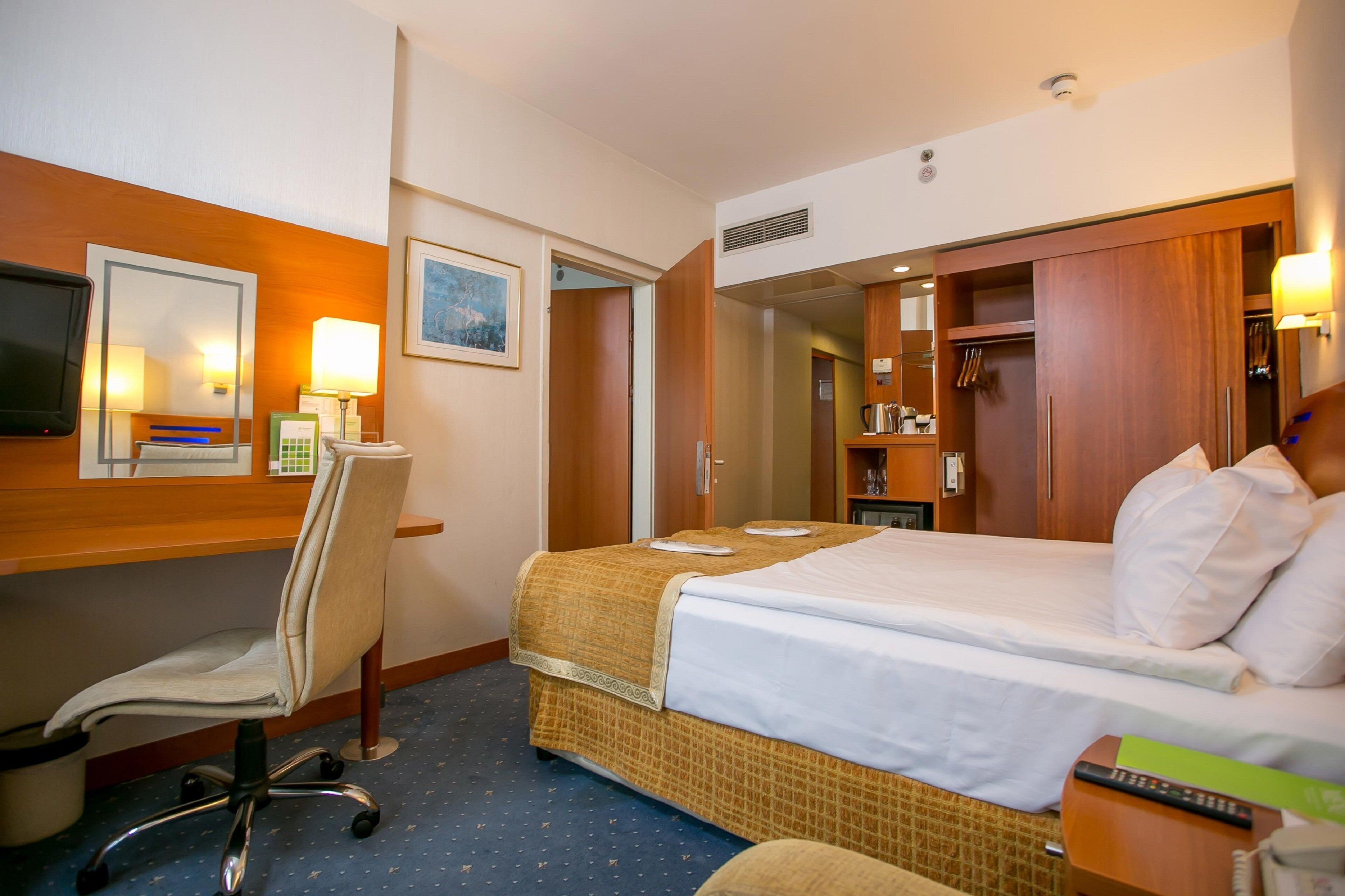 A hotel room with a bed, desk, chair, and a wardrobe.