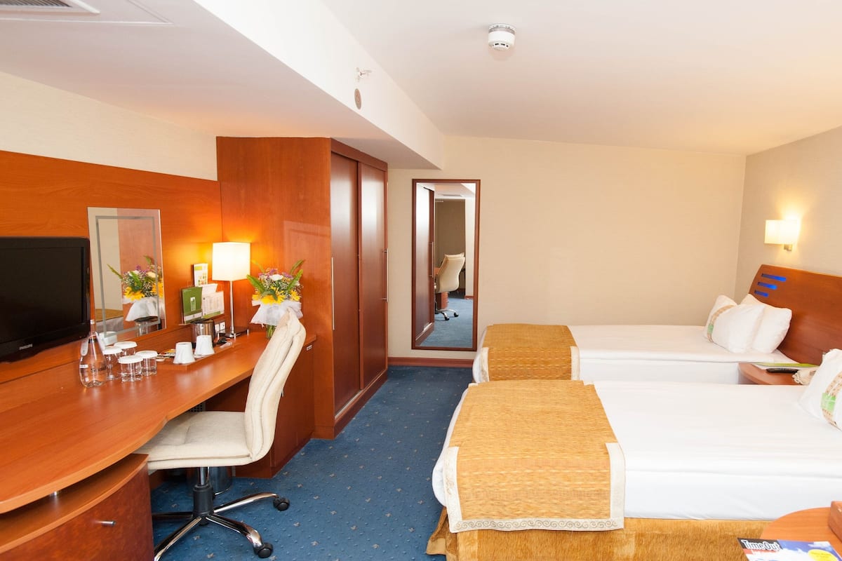 Hotellihuone, jossa on työpöytä, kaksi sänkyä, televisio ja peili.