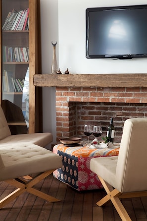 Una sala de estar acogedora con chimenea de ladrillo, un televisor de pantalla plana montado arriba y dos sillones cómodos.