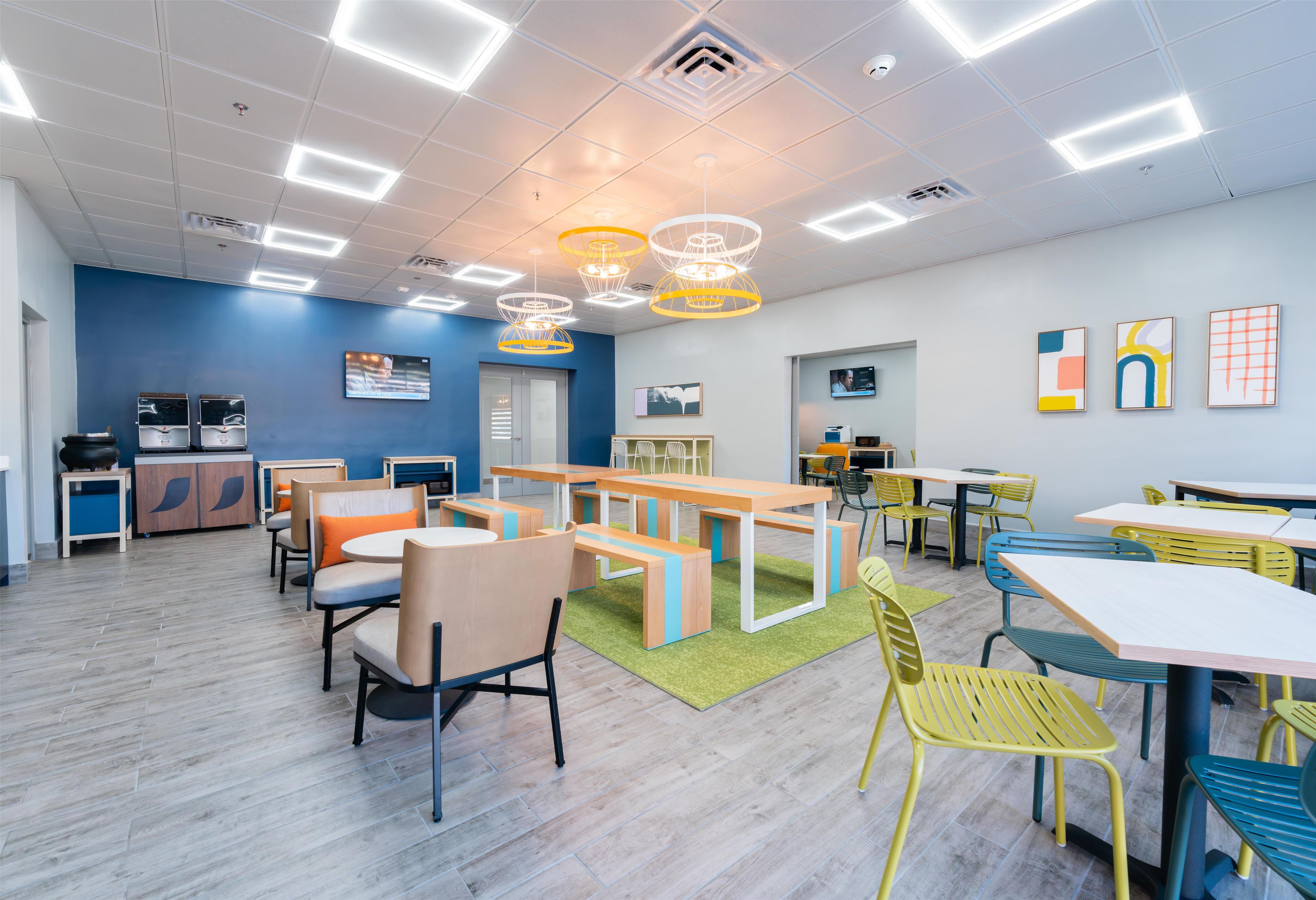 Un espace intérieur moderne doté de plusieurs coins salon, comprenant des tables et des chaises, ainsi qu’un téléviseur fixé au mur.
