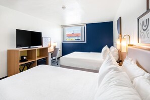 A hotel room with two beds, a TV, a desk, and a window with a view of buildings. - Spark by Hilton Ponce (Ponce)