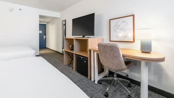Habitación de hotel con cama, escritorio, silla, televisor, lámpara y un cuadro en la pared.
