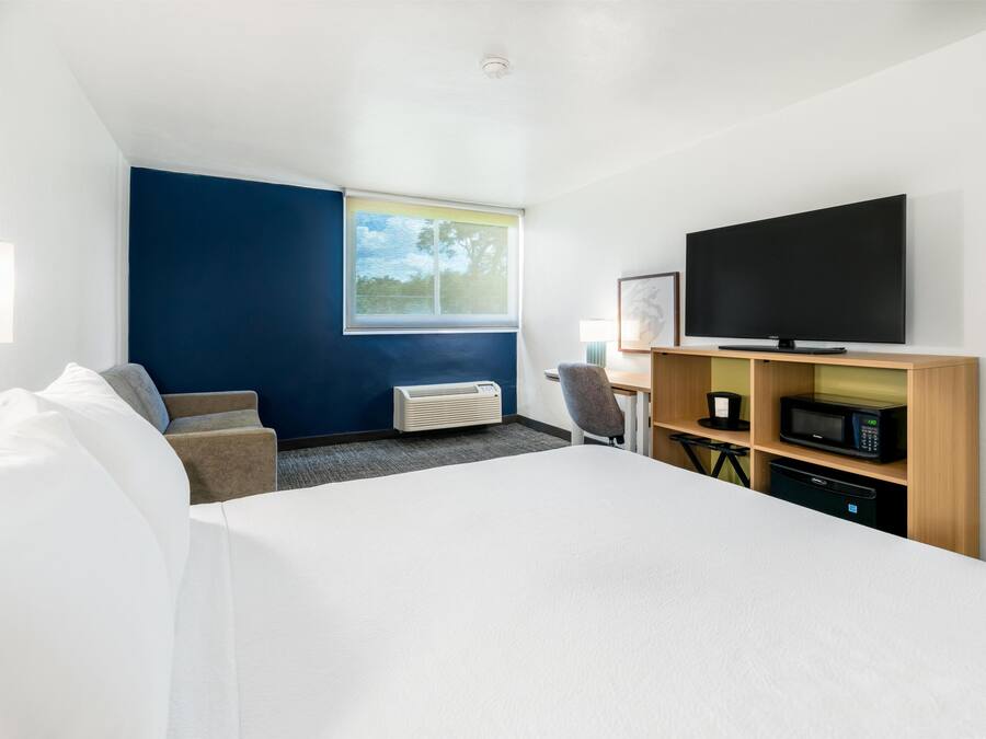 Ein Hotelzimmer mit einem großen Bett, einem Flachbildfernseher, einem Schreibtisch mit eingebauter Mikrowelle und einem Fenster mit Blick auf Bäume.