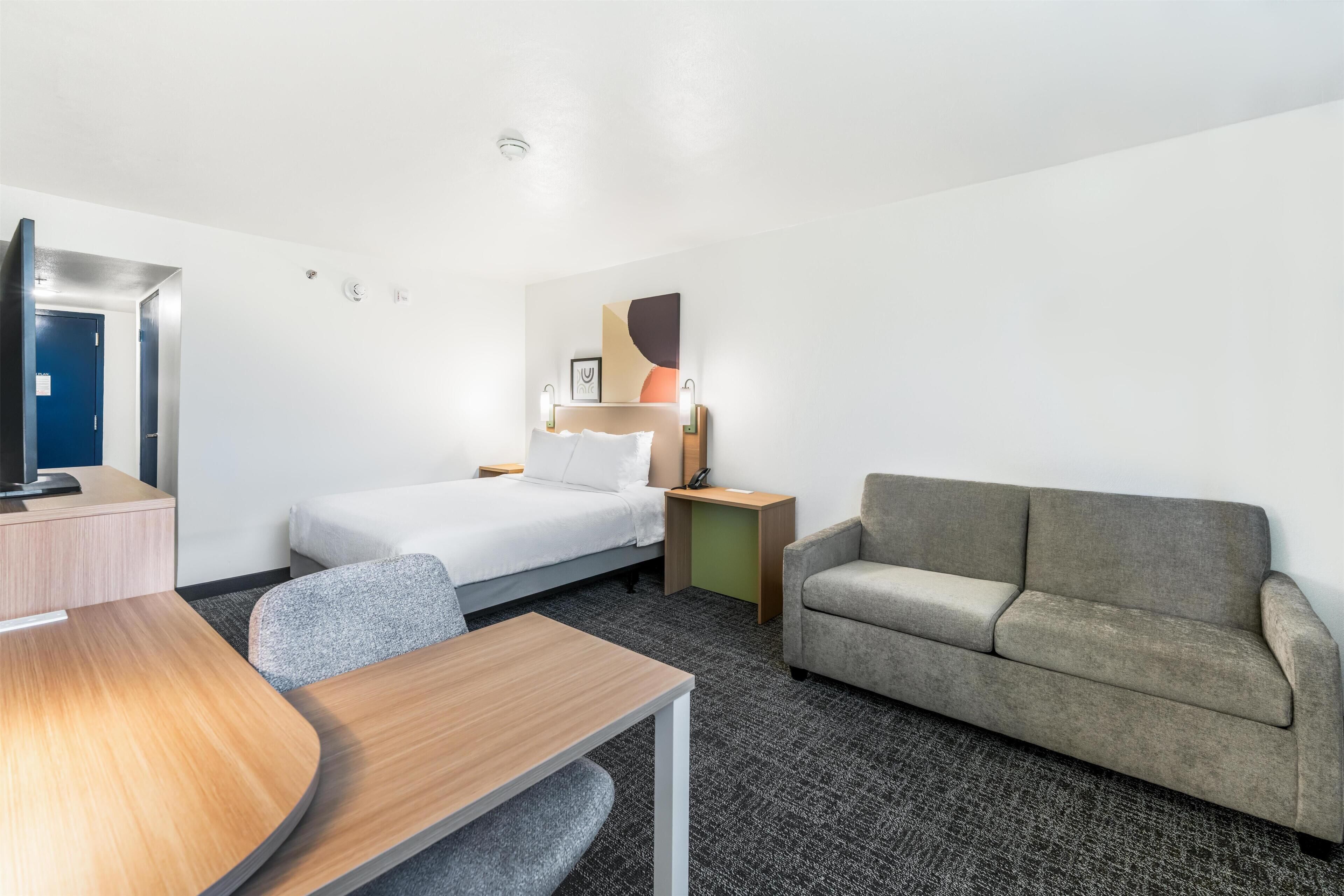 A hotel room with a bed, a desk, a sofa, and a small table.