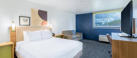 A hotel room with a bed, a desk, a chair, a TV, and a window with a view.