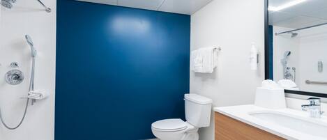 A modern bathroom with a white toilet, a blue accent wall, a shower with a handheld showerhead, and a large mirror above the sink.