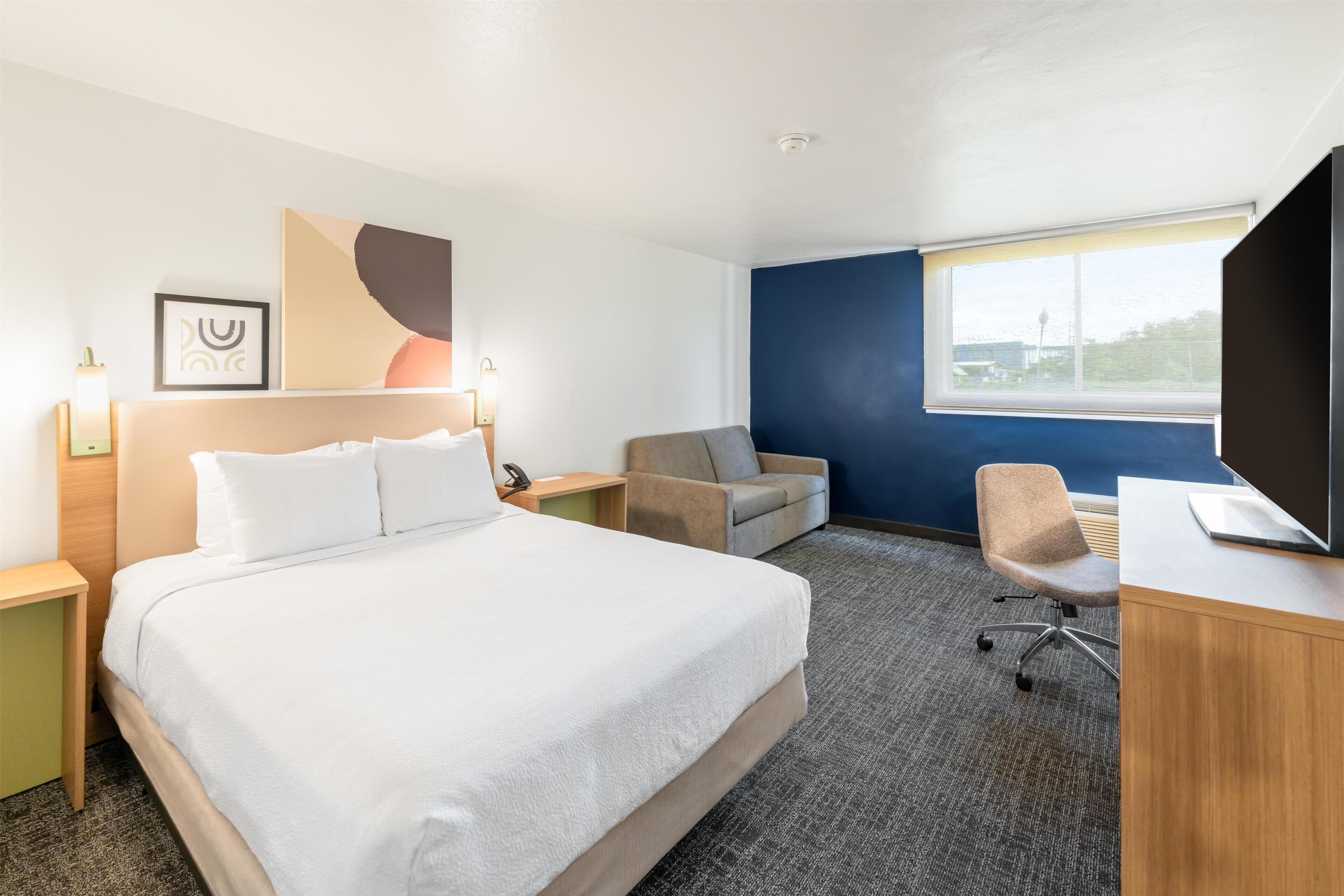 A hotel room with a bed, a desk, a chair, a TV, and a window.