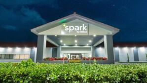 L’entrée d’un hôtel, avec une enseigne indiquant « Spark by Hilton », un espace abrité éclairé et un banc.