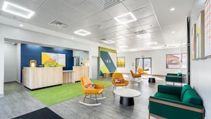 Un espace de bureau moderne comprenant un comptoir d’accueil, un coin salon et une moquette verte.