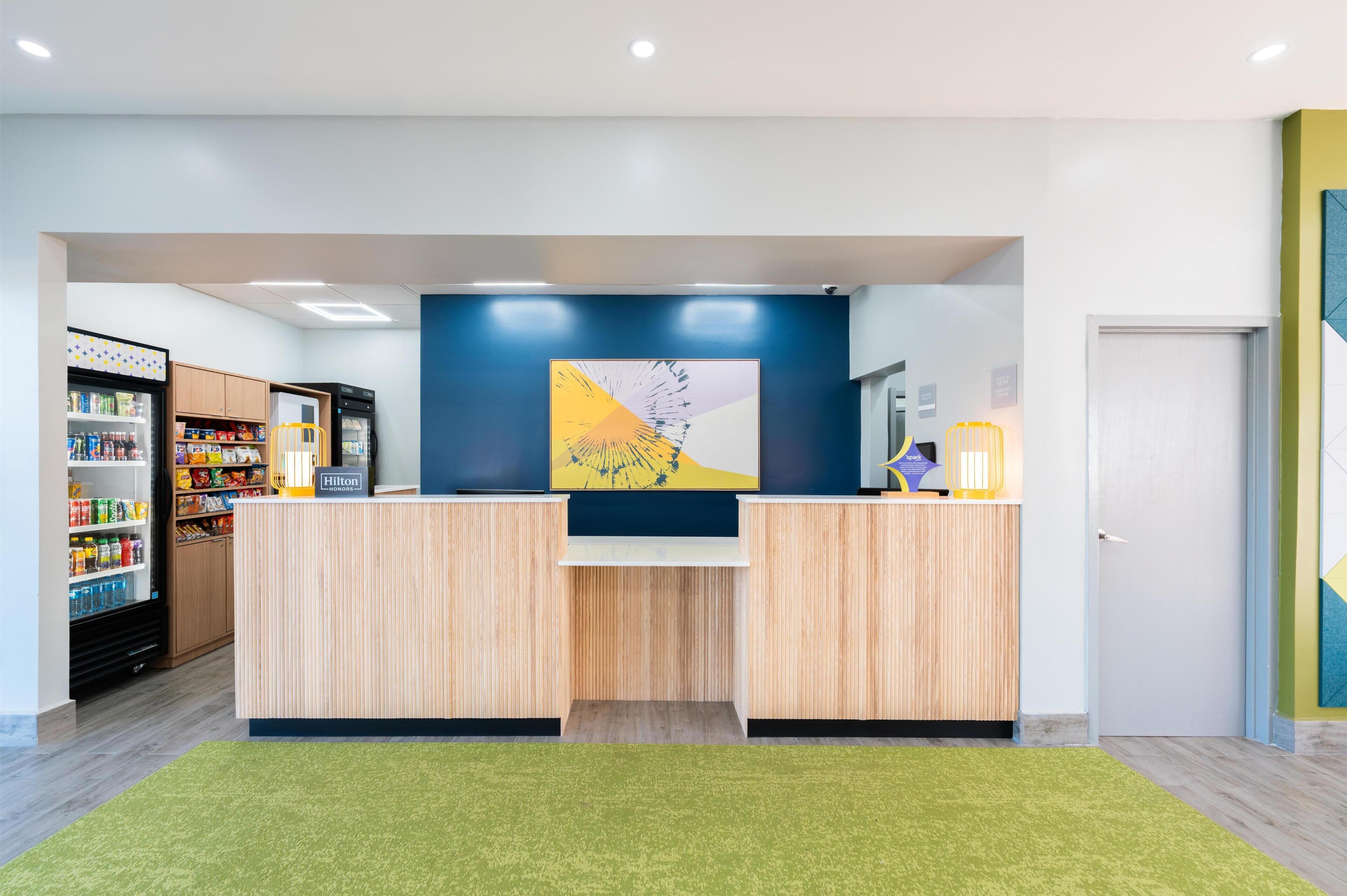 Un mostrador de recepción de hotel con una pared azul, un cuadro abstracto grande y una alfombra verde.