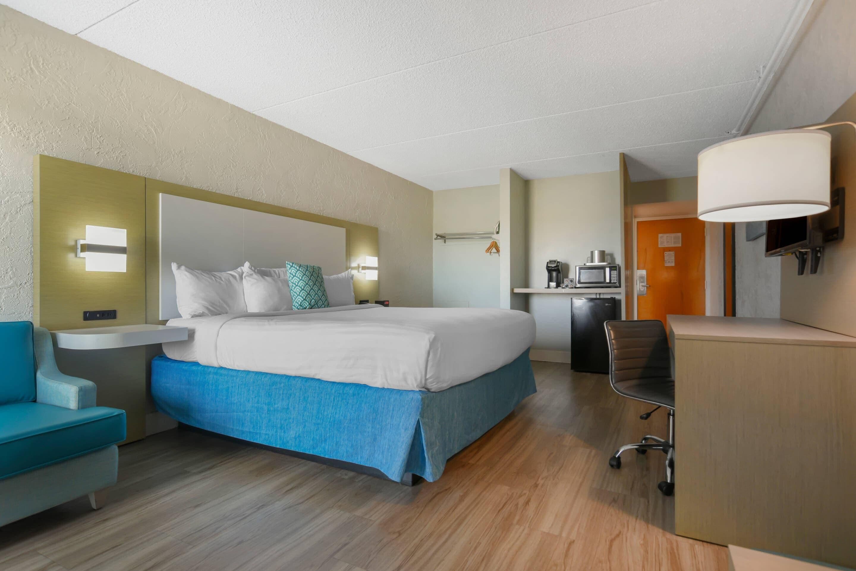 Een hotelkamer met een bed, een bureau, een stoel, een magnetron en een koffiezetapparaat.