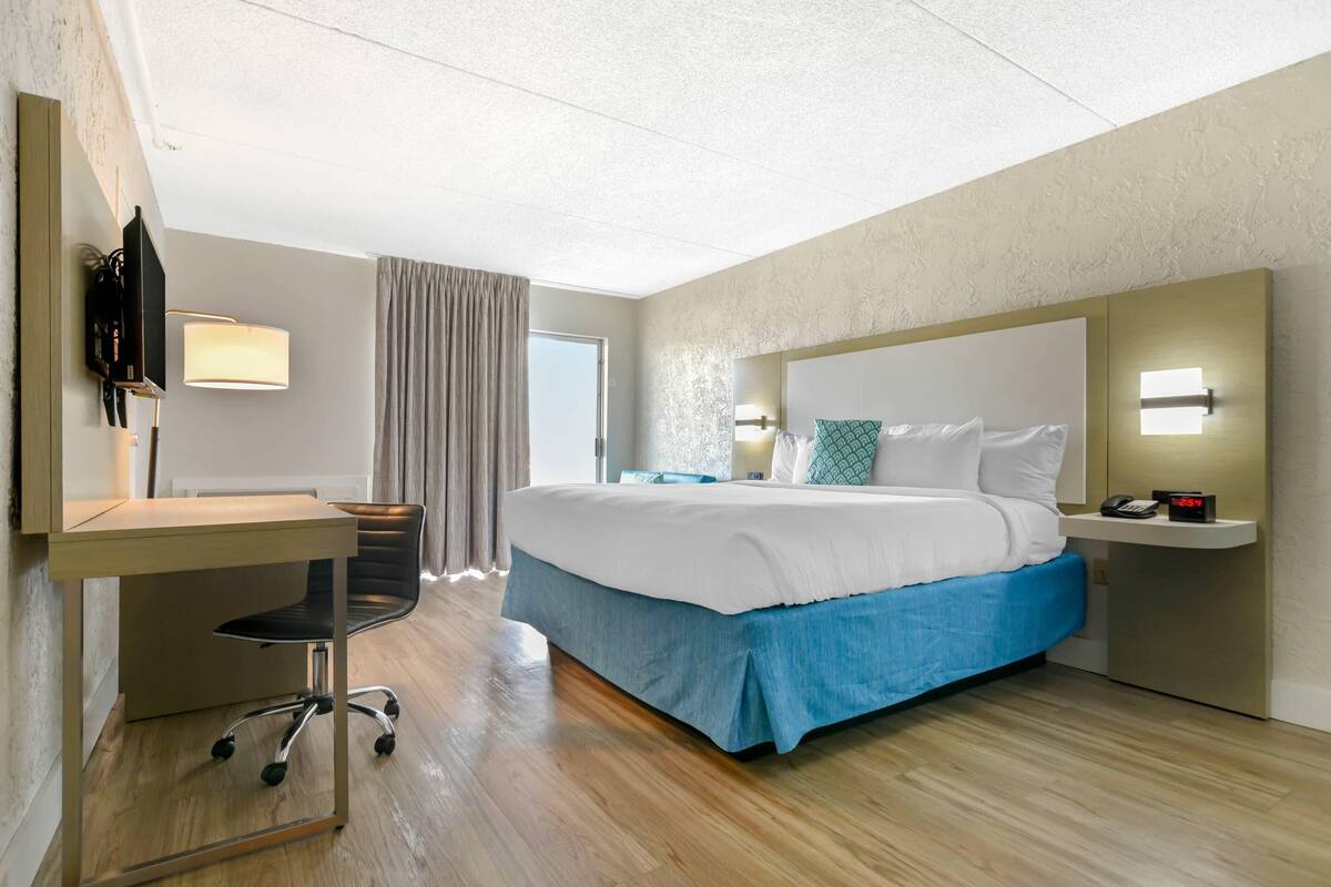 Habitación de hotel con cama, escritorio, silla y televisor.
