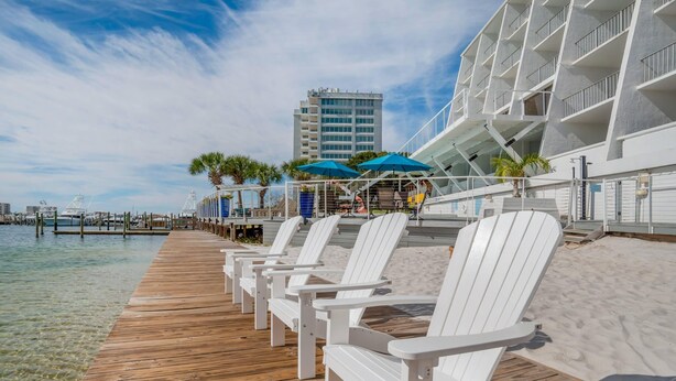 A wooden pier with white chairs, a building with balconies, and a clear view of the water. - Inn on Destin Harbor, an Ascend Collection Hotel (Destin)