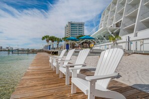 A wooden pier with white chairs, a building with balconies, and a clear view of the water. - Inn on Destin Harbor, an Ascend Collection Hotel (Destin)