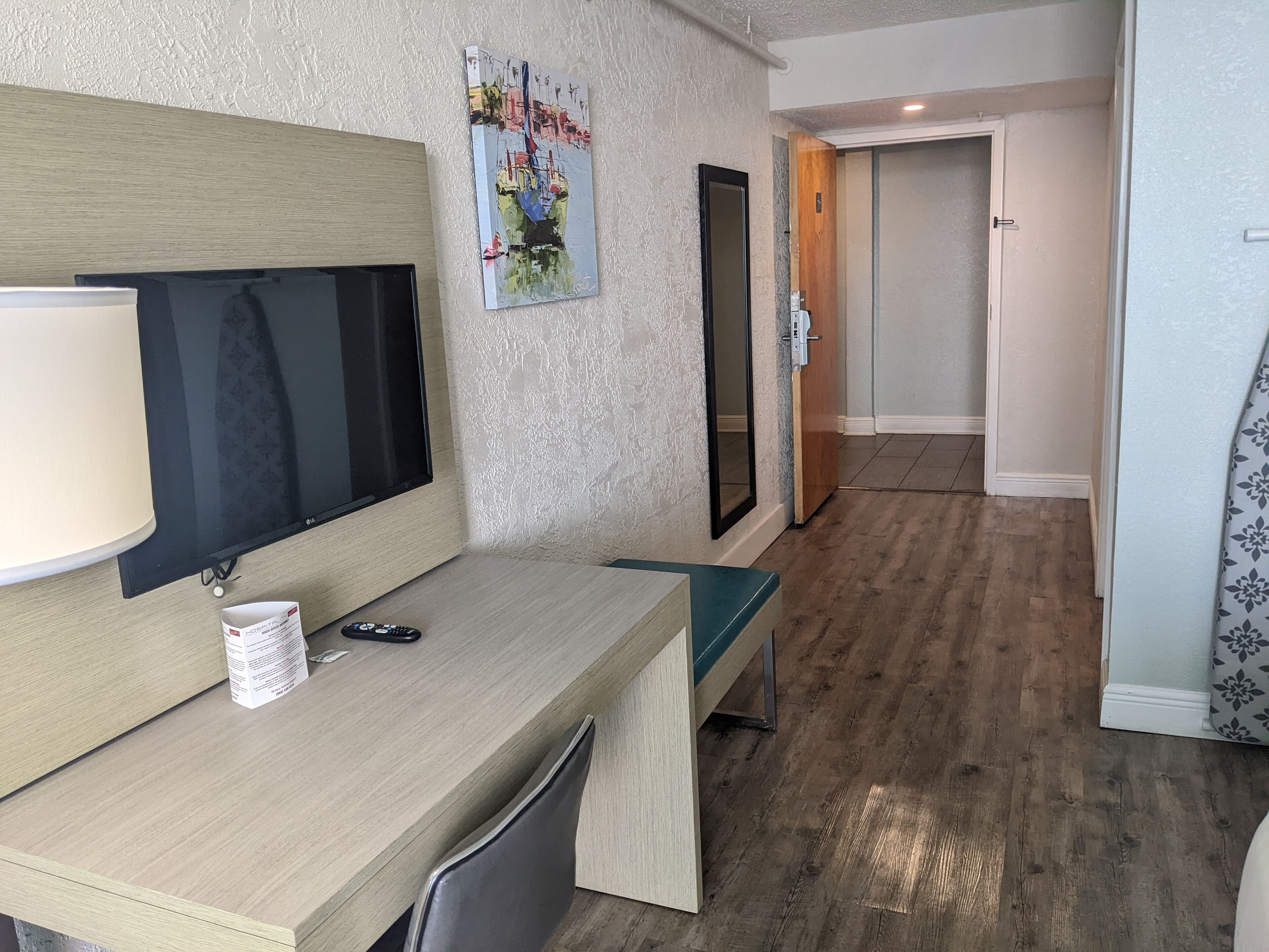Habitación de hotel con un escritorio de madera, un televisor de pantalla plana, un espejo y una puerta que da a otra habitación.