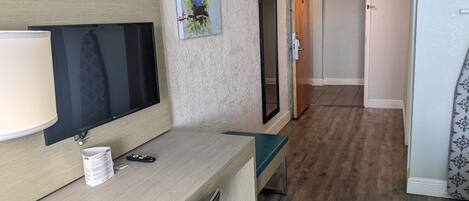 Habitación de hotel con un escritorio de madera, un televisor de pantalla plana, un espejo y una puerta que da a otra habitación.