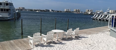 A marina with a sandy beach, white chairs, and a docked boat.