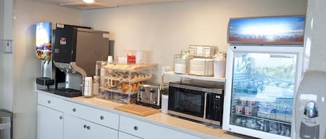 Een kitchenette met een koffieapparaat, broodrooster, magnetron en koelkast.