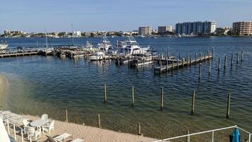 A marina with boats docked, a sandy beach with lounge chairs, and buildings in the background.