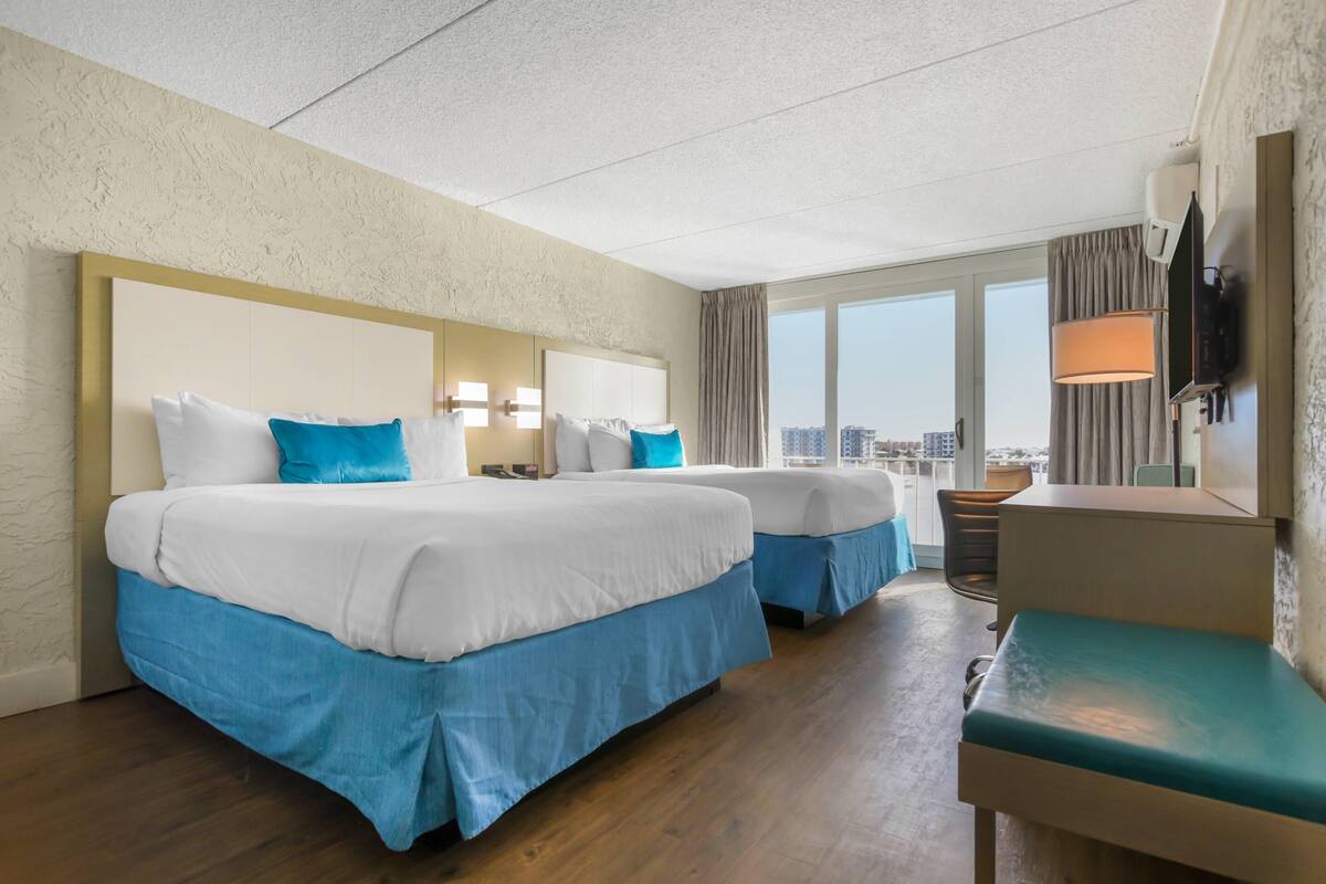 Habitación de hotel con dos camas, un escritorio, una silla y un ventanal grande.