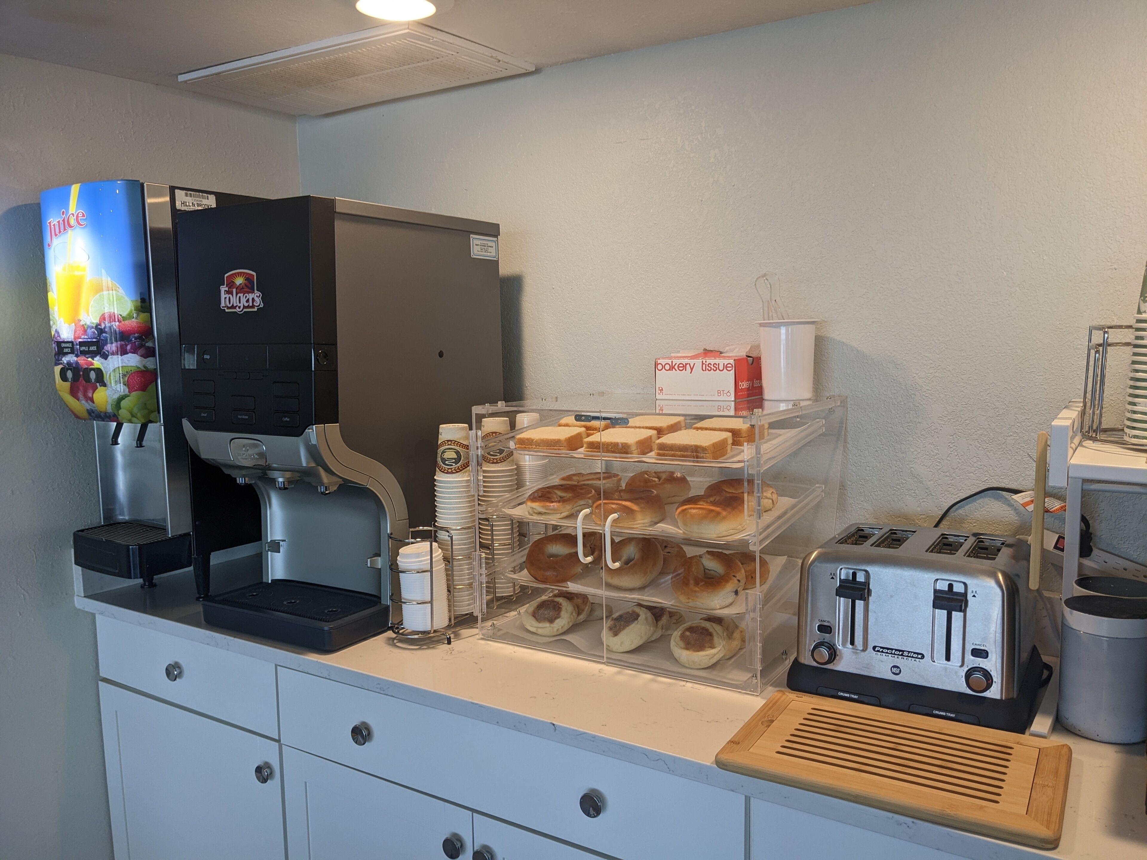 A breakfast station with a juice dispenser, a coffee machine, a bread display, and a toaster.