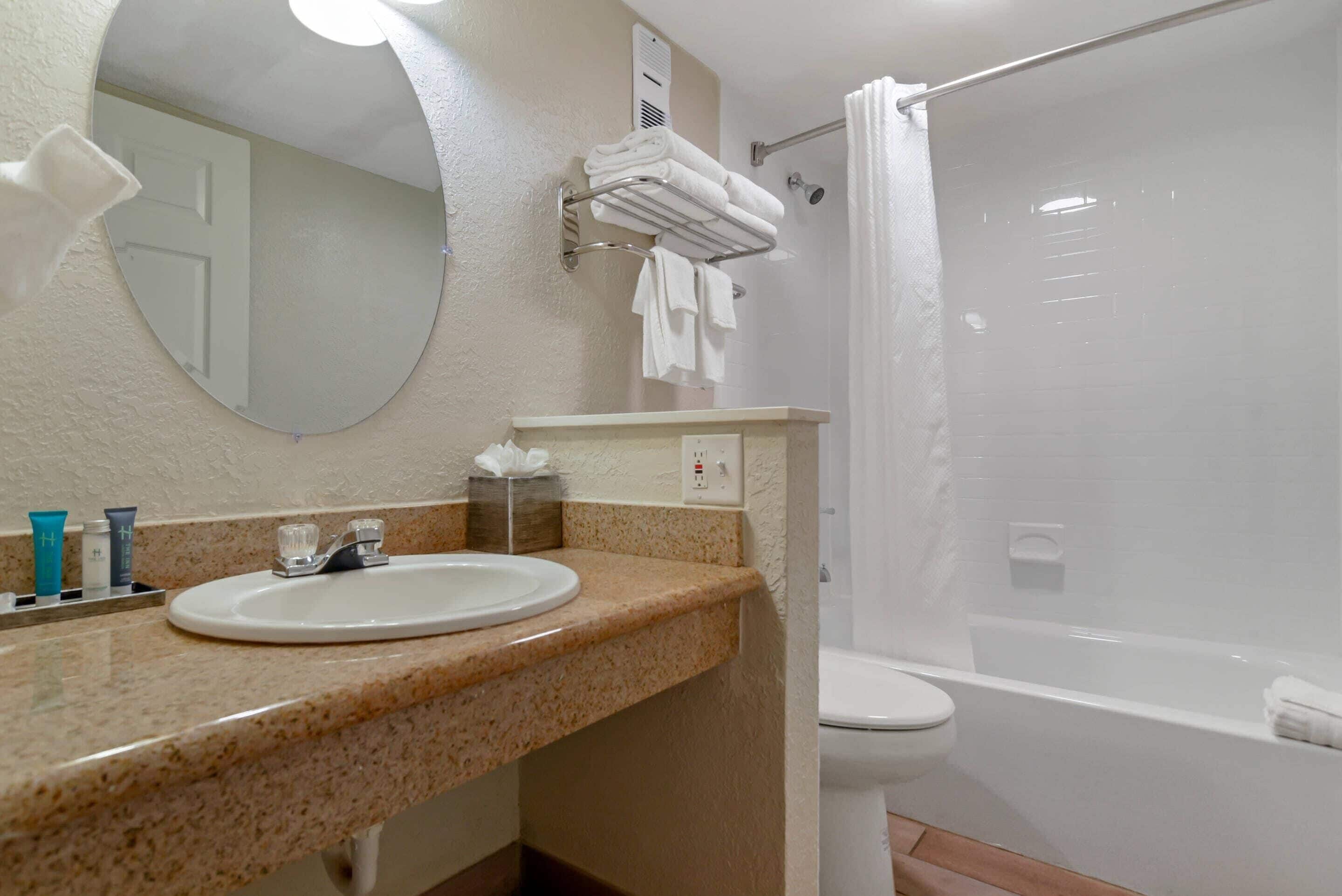A bathroom with a sink, mirror, towel rack, shower, and toilet.