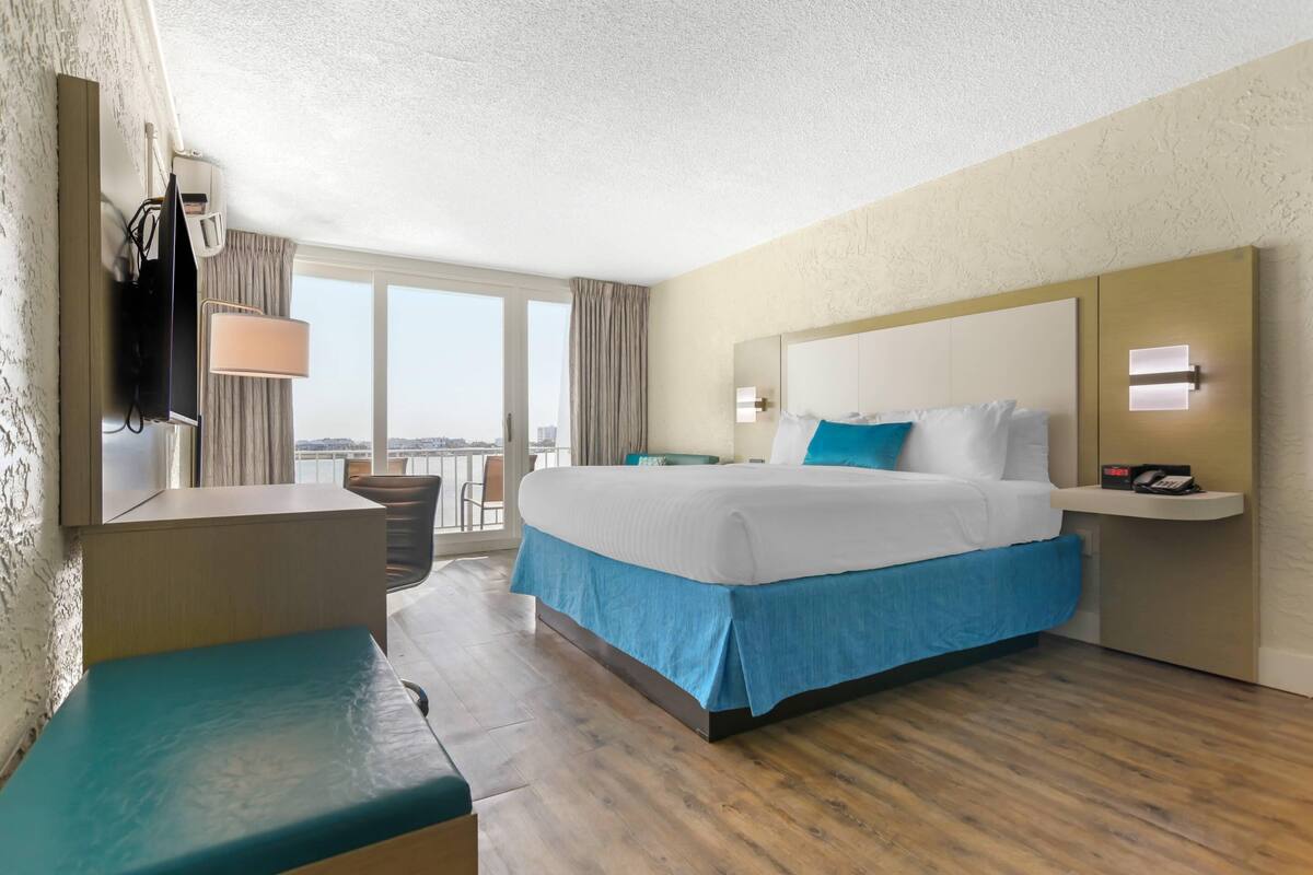 Una habitación de hotel con cama, escritorio, silla, televisor y vista a la ciudad.