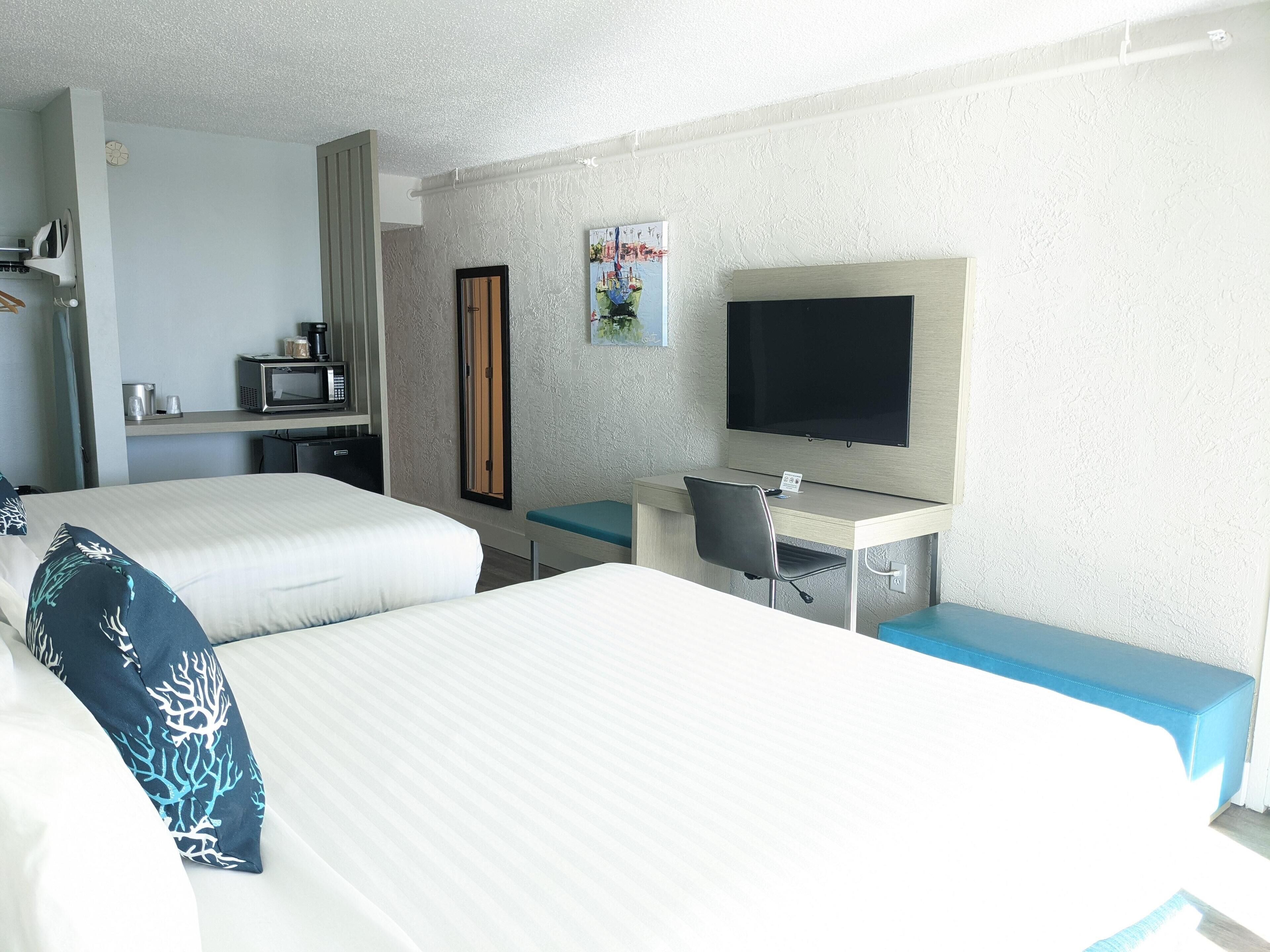 A hotel room with two beds, a desk with a chair, a television, and a small kitchenette.
