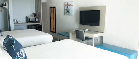 A hotel room with two beds, a desk with a chair, a television, and a small kitchenette.