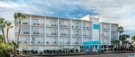 A multi-story hotel with balconies, a parking lot, and a blue awning.