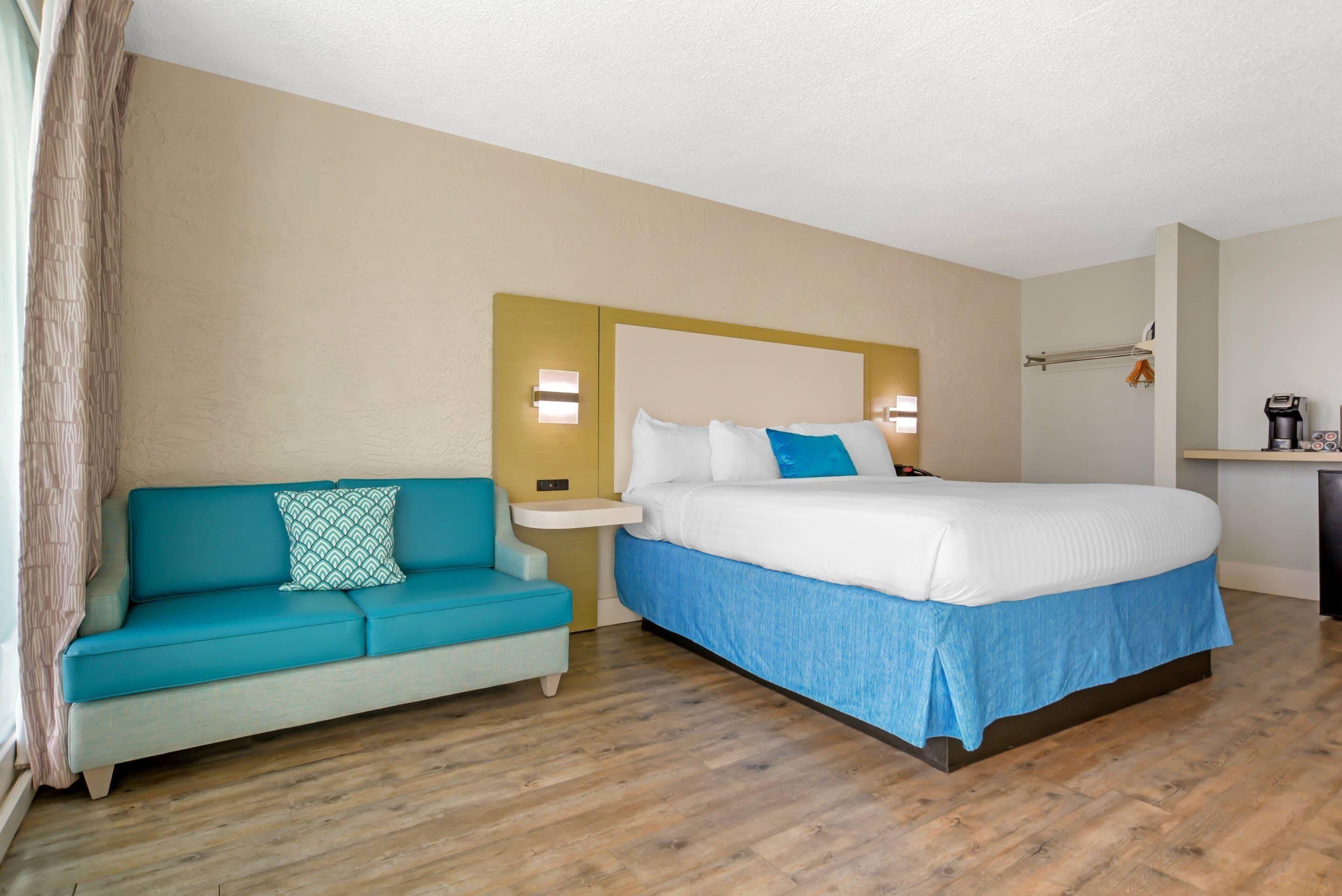 A hotel room with a bed, a sofa, a nightstand, and a mirror.