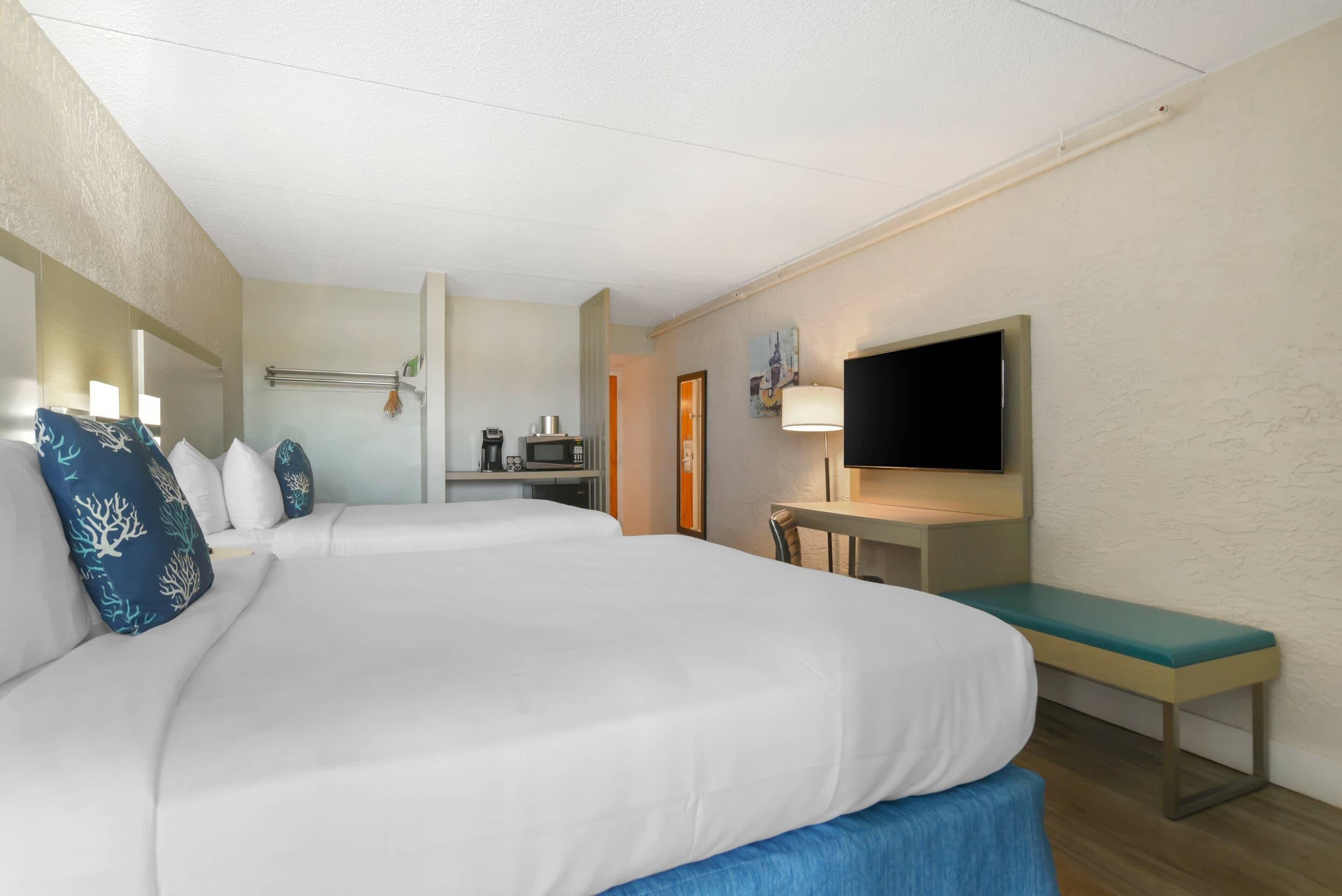 A hotel room with two beds, a desk, a television, and a bathroom.