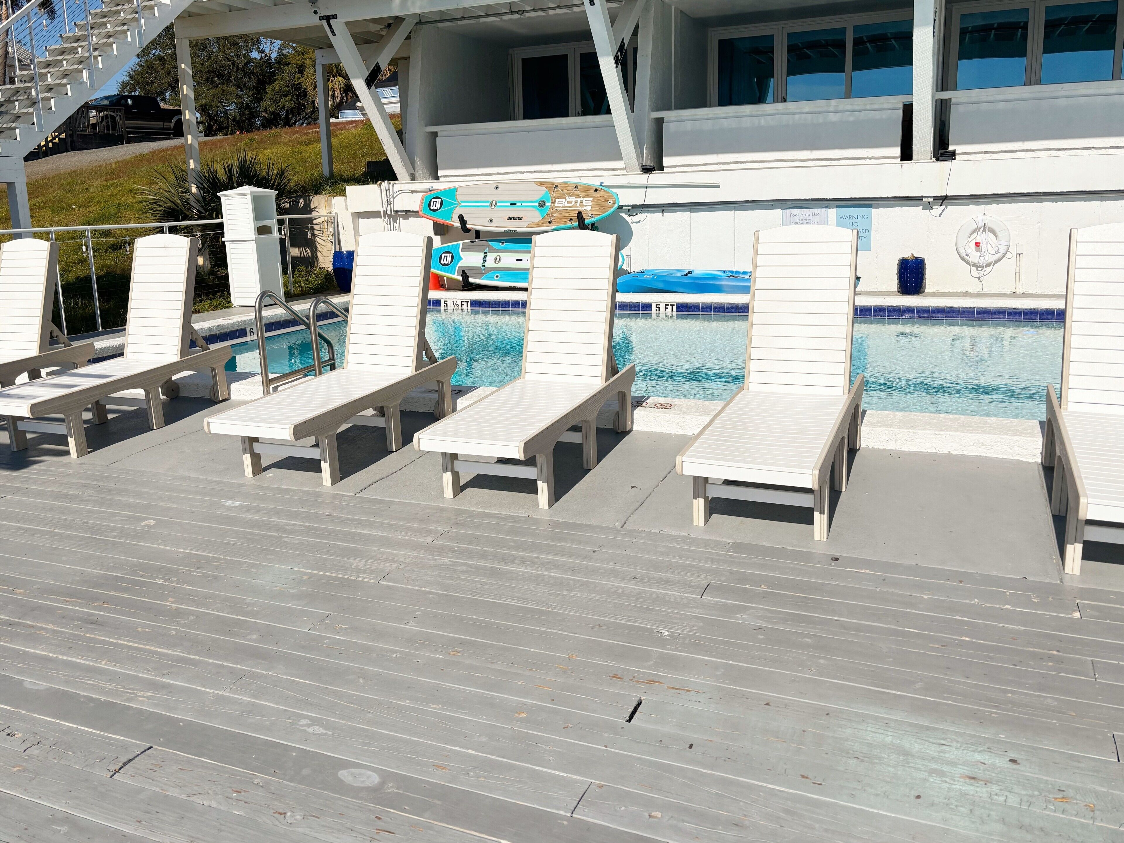 A poolside area with lounge chairs and a sign indicating a 5 ft depth.