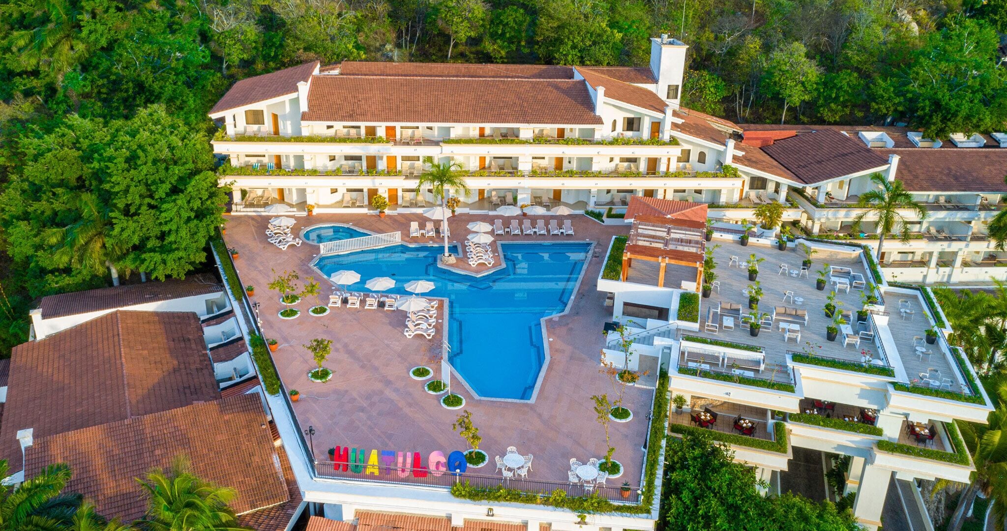 Un hotel grande con varios pisos, una piscina central y zonas de estar al aire libre.