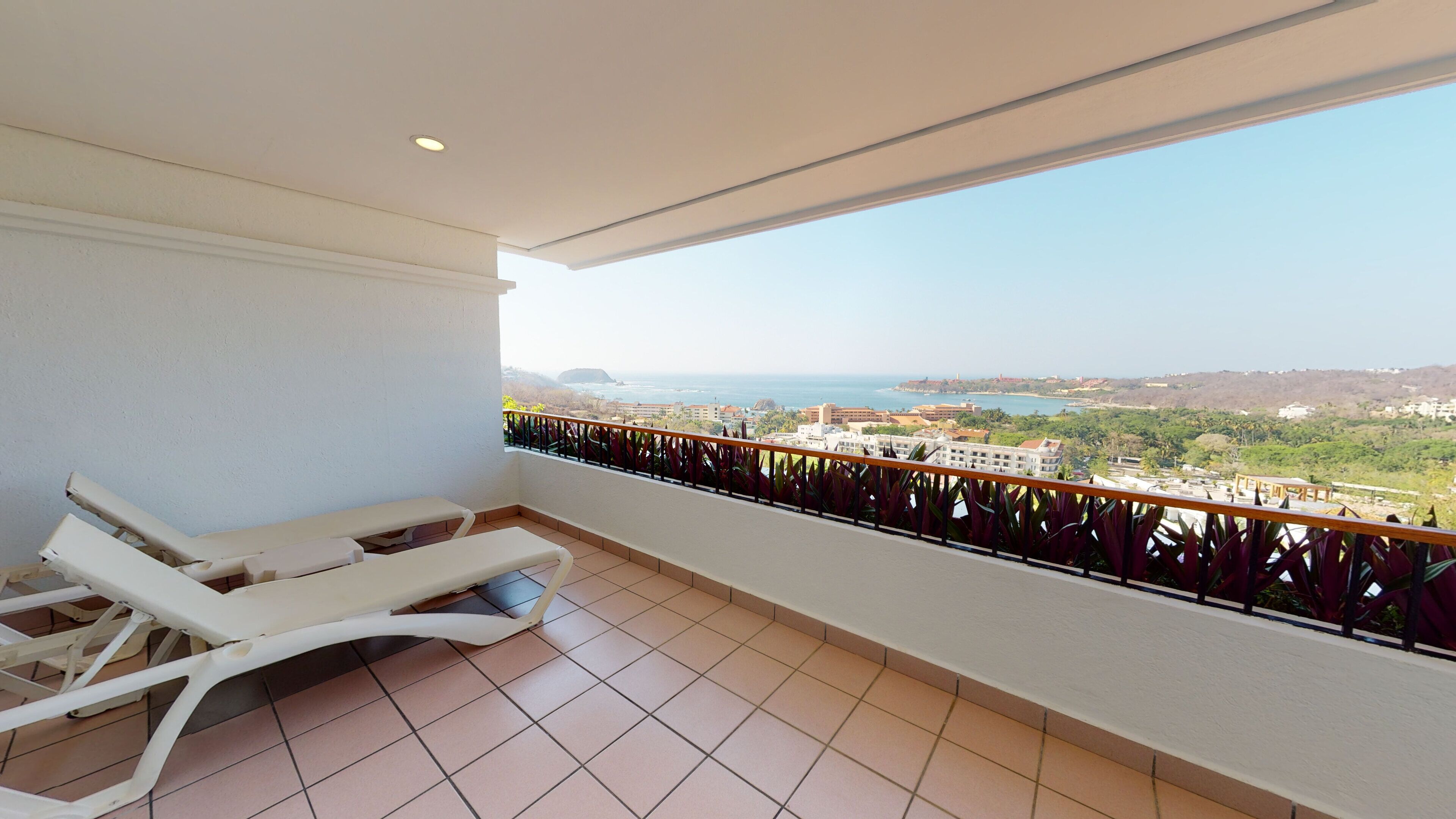 A balcony with two white sun loungers, a view of the sea, and a tiled floor.