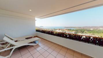 A balcony with two white sun loungers, a view of the sea, and a tiled floor.