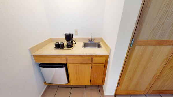 A small kitchenette with a sink, a coffee maker, and a trash can.
