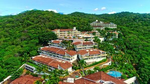 A multi-story hotel with a pool, surrounded by lush greenery and hills.