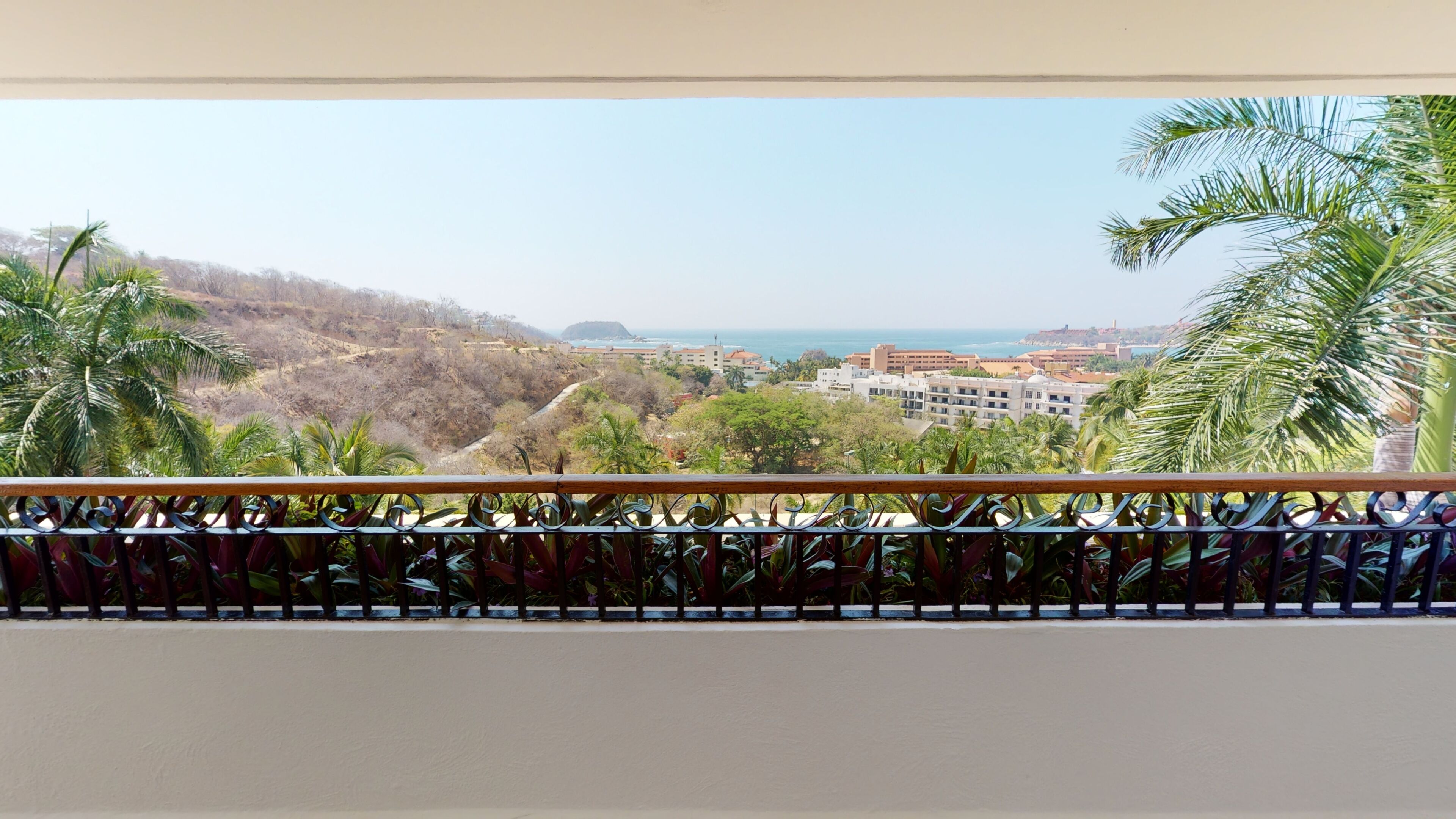 Un balcón con vistas a un paisaje costero, que incluye edificios y palmeras.