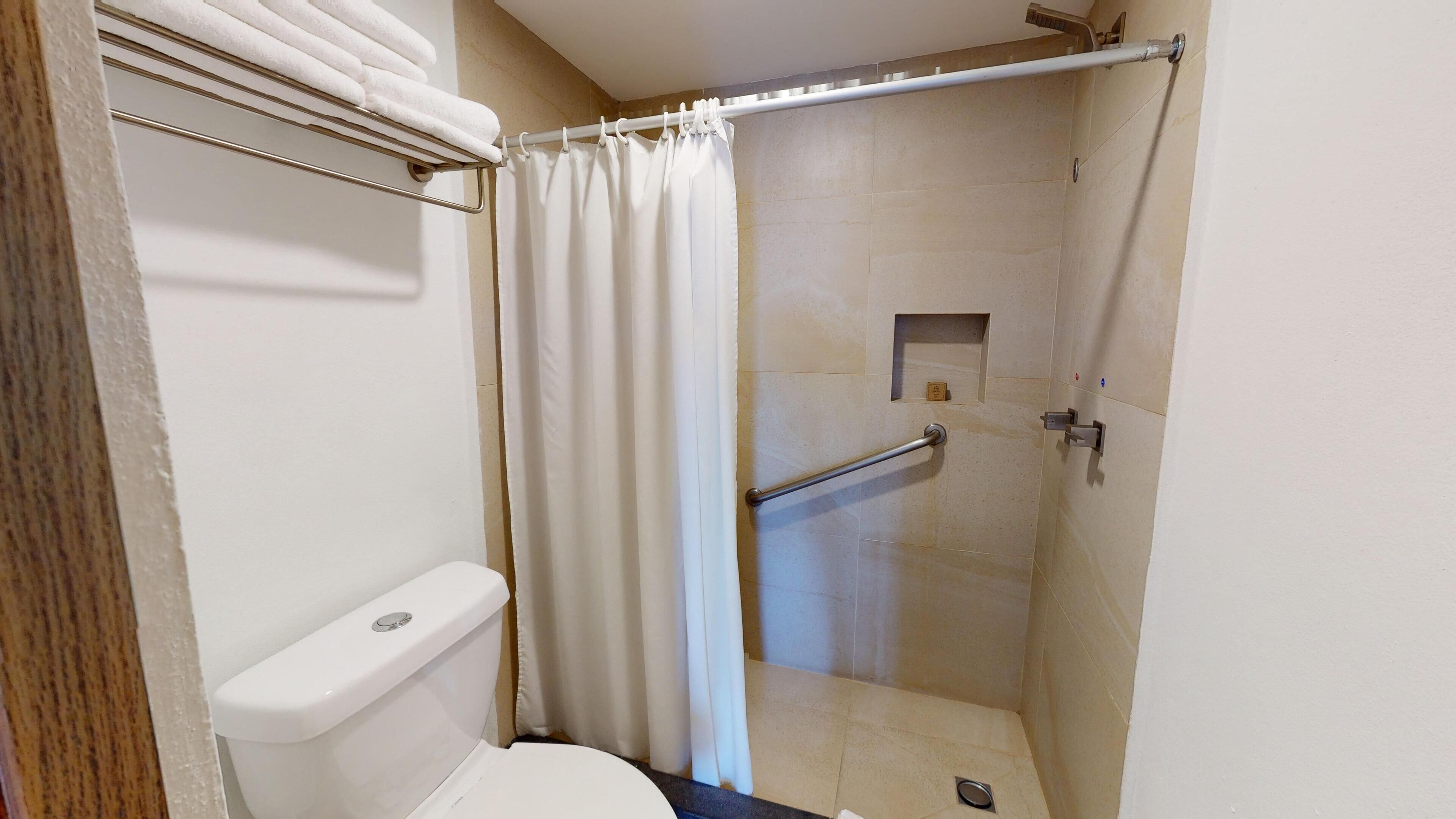 A small, enclosed shower stall with a toilet, a towel rack, and a shower curtain.