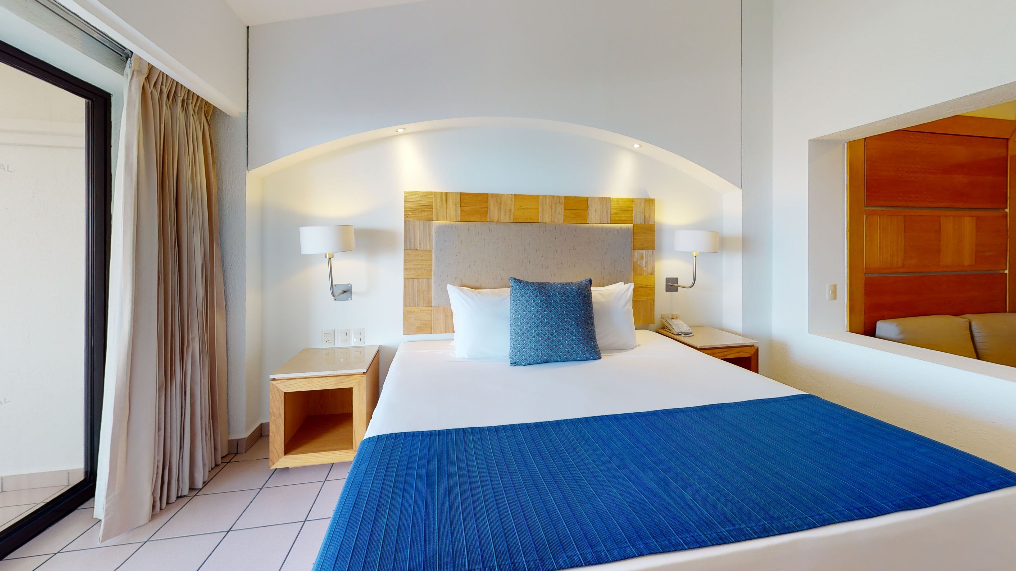 A hotel room with a large bed, two bedside tables, a wooden headboard, and a large mirror.