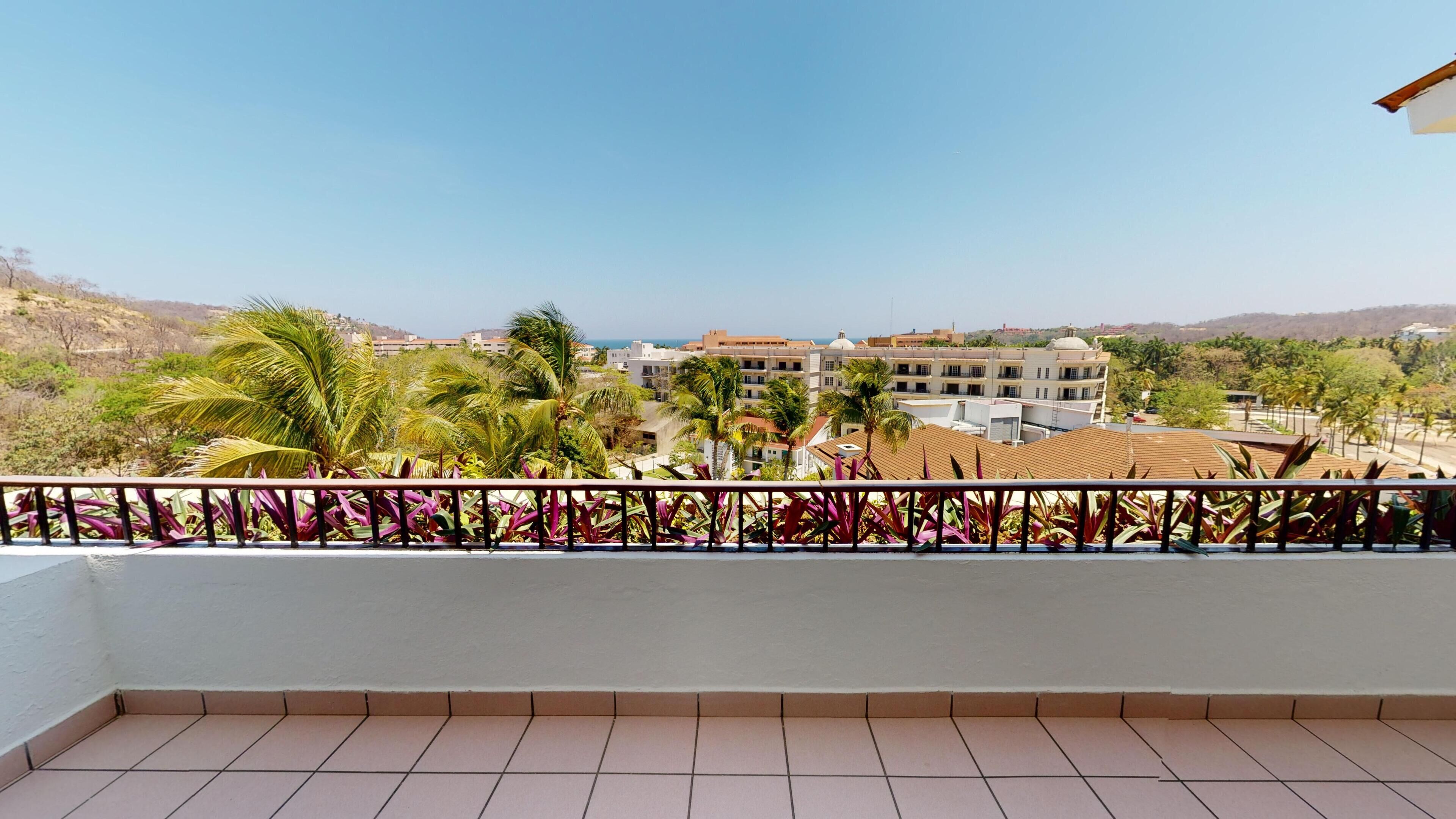 Un balcon doté d’un sol carrelé, d’une rambarde en métal et offrant une vue sur un ensemble d’immeubles à plusieurs étages, agrémenté de palmiers.