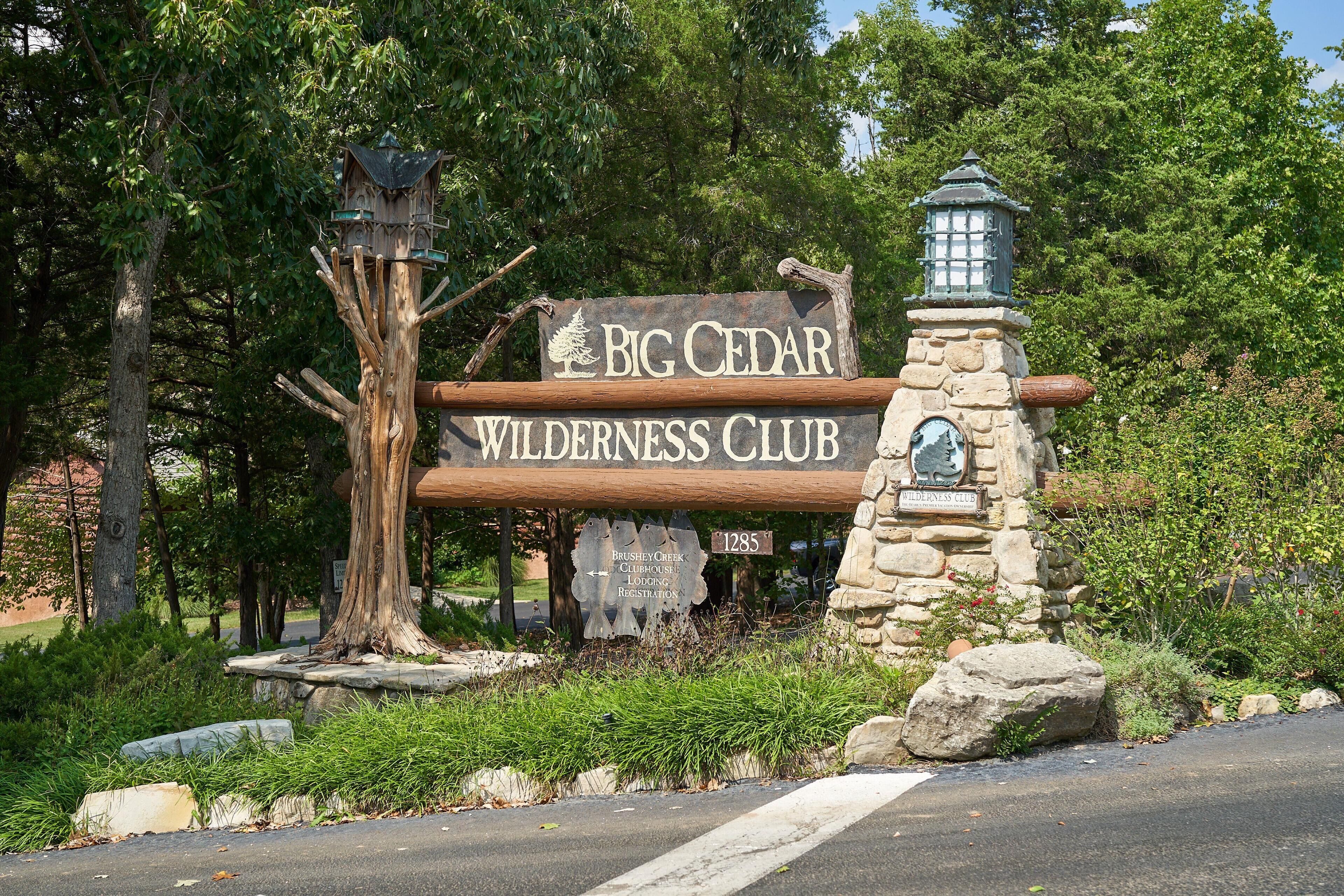 Un letrero de madera del Big Cedar Wilderness Club, con un farolillo de piedra rústico y un comedero para pájaros.