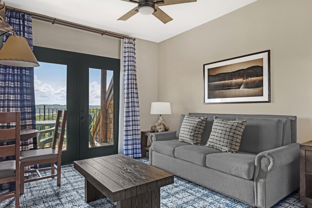 A room with a grey sofa, a wooden coffee table, a lamp, and a framed picture on the wall.