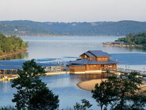 A lakeside lodge with a wooden exterior, dock, and a view of the lake and surrounding hills. - Hilton Grand Vac Club Wilderness Club at Big Cedar Ridgedale (Ridgedale)
