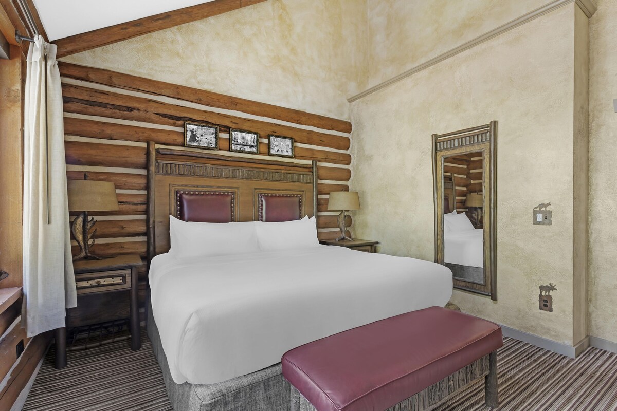 A log cabin-style bedroom with a large bed, wooden headboard, and a mirror.